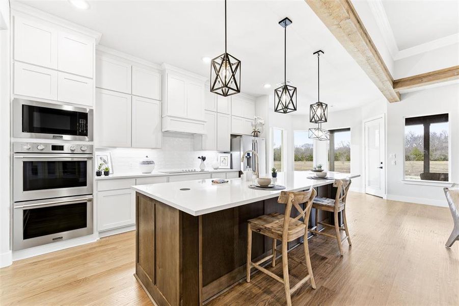 Kitchen with white cabinetry, stainless steel appliances, a kitchen breakfast bar, pendant lighting, and a center island with sink