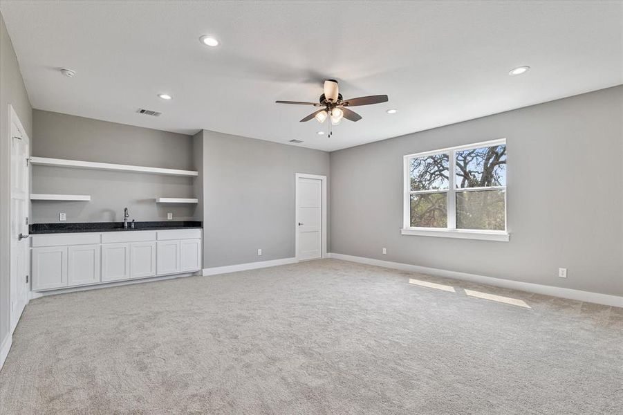 Unfurnished living room featuring sink, ceiling fan, and light colored carpet