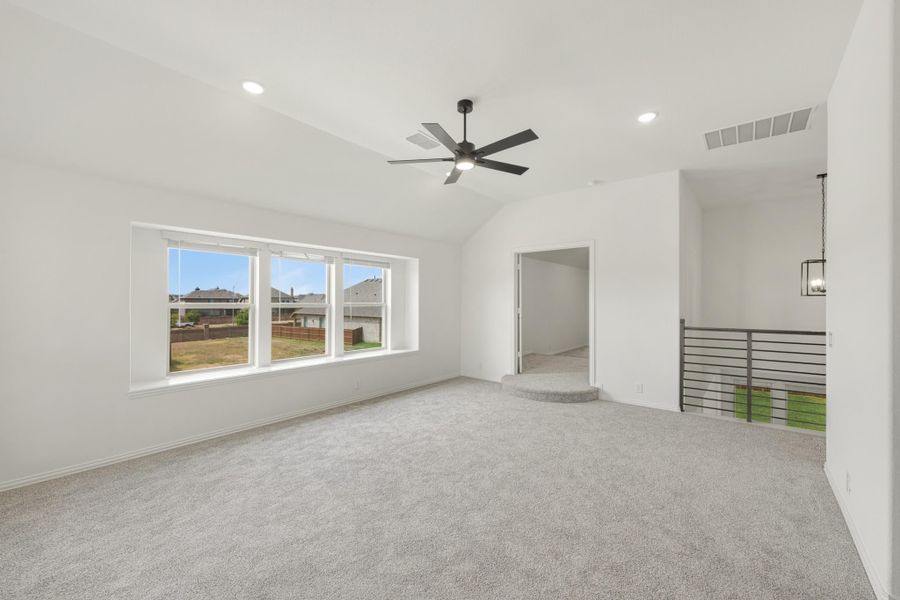 Empty bedroom with vaulted ceiling, ceiling fan, carpet flooring, and large windows overlooking backyard