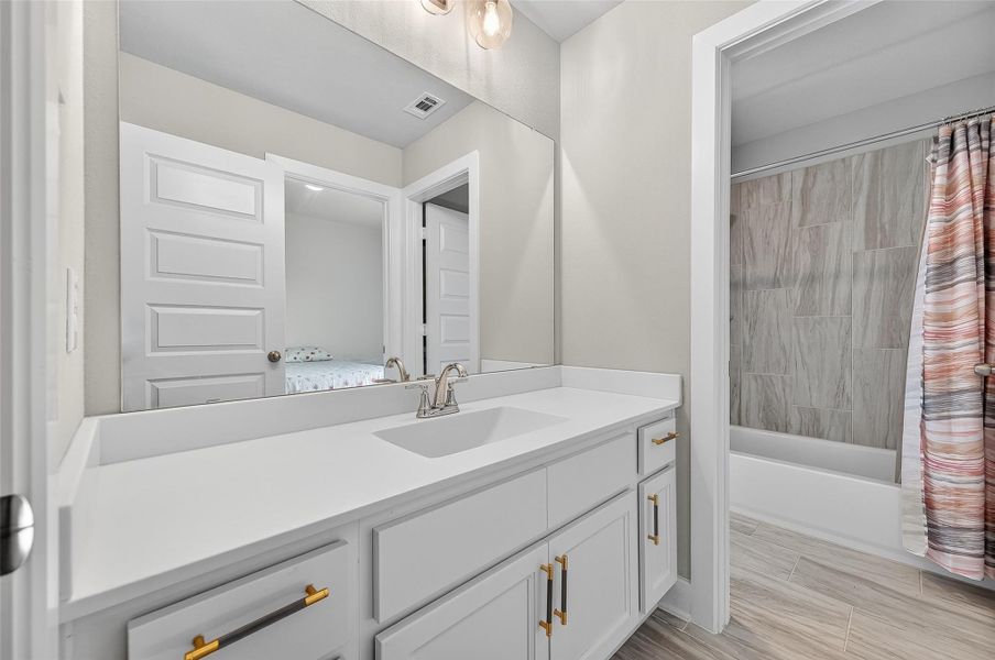 Stylish secondary bathroom featuring a dual-sink vanity with quartz countertops and modern brass hardware. The separate shower/tub combo offers convenience and privacy for shared use.