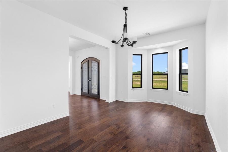 Empty room with a chandelier, dark wood-type flooring, and french doors Empty room with a chandelier, dark wood-type flooring, and french doors