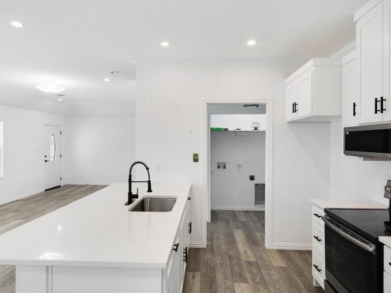 Kitchen featuring a large island with an undermount sink and matte black faucet, white cabinetry with black hardware, and wood-finish flooring