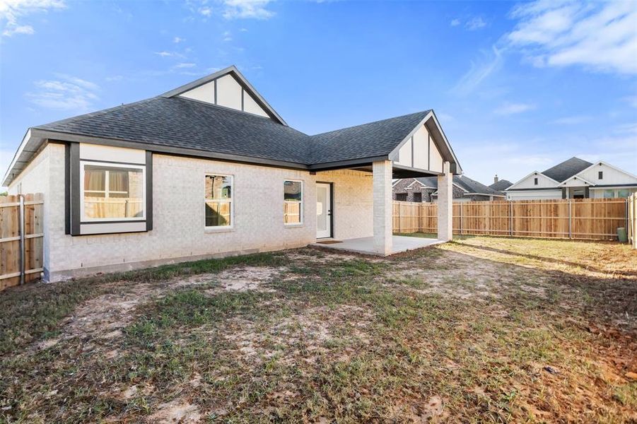 Rear view of property featuring a shingled roof, a patio area, a fenced backyard, and brick siding