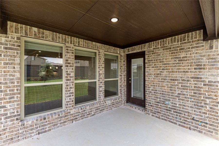 Covered back patio with brick exterior, large windows, and dark door leading to backyard Covered back patio with brick exterior, large windows, and dark door leading to backyard
