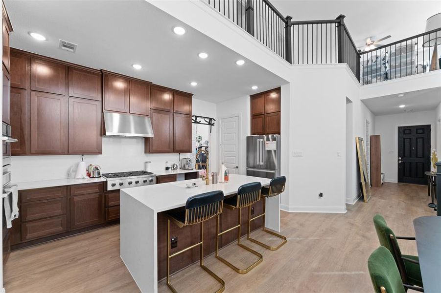 Kitchen featuring a breakfast bar, a high ceiling, a kitchen island with sink, recessed lighting, and light wood-style floors Kitchen featuring a breakfast bar, a high ceiling, a kitchen island with sink, recessed lighting, and light wood-style floors