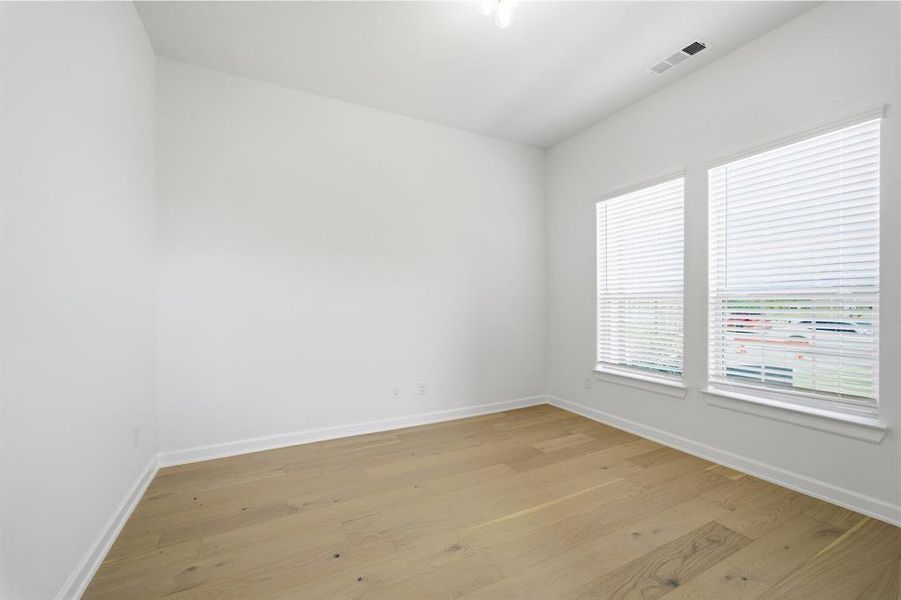 Spacious room featuring light wood-finish flooring, white walls, and two large windows with blinds