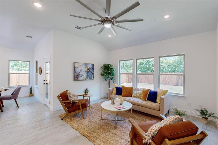 Living room featuring light wood-type flooring, a wealth of natural light, vaulted ceiling, and ceiling fan