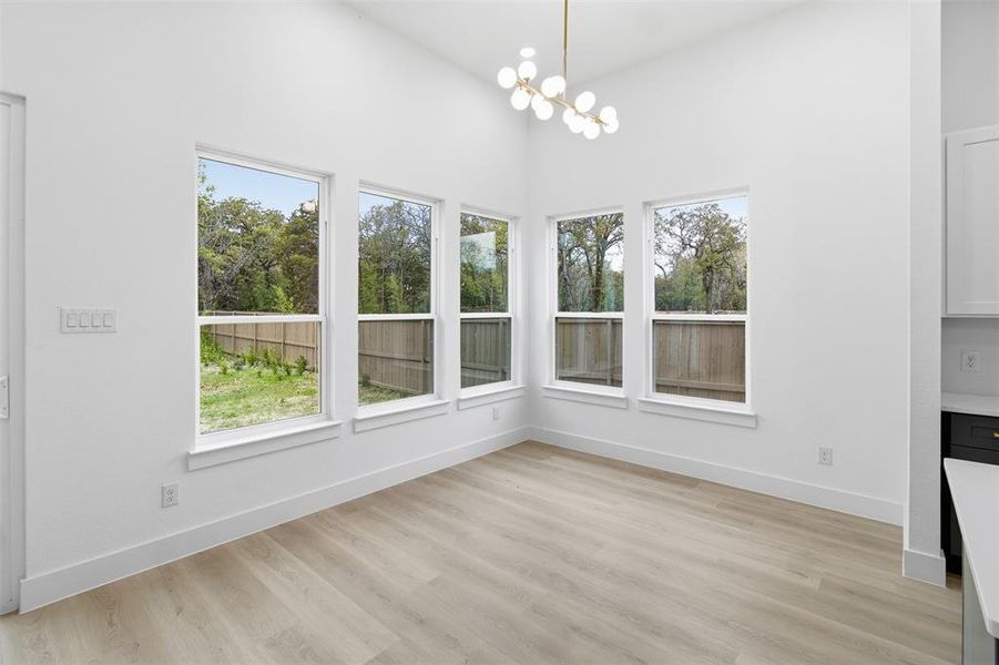 Unfurnished dining area featuring plenty of natural light, a chandelier, light wood-type flooring, and a towering ceiling