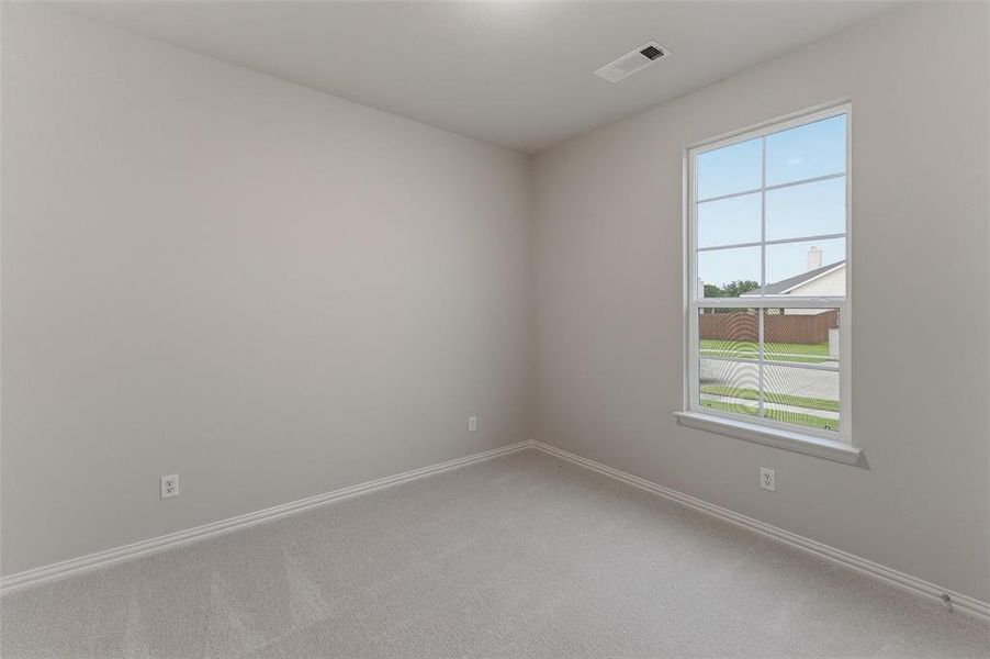 Neutral-toned room featuring a large window with grid pattern, light gray carpeting, matching baseboards, and a ceiling-mounted light fixture Neutral-toned room featuring a large window with grid pattern, light gray carpeting, matching baseboards, and a ceiling-mounted light fixture