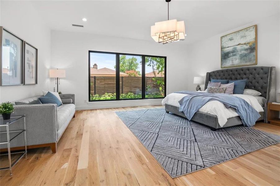 Spacious room featuring light wood-finish flooring, a large multi-pane window with black framing, recessed lighting, and a contemporary ceiling fixture Spacious room featuring light wood-finish flooring, a large multi-pane window with black framing, recessed lighting, and a contemporary ceiling fixture