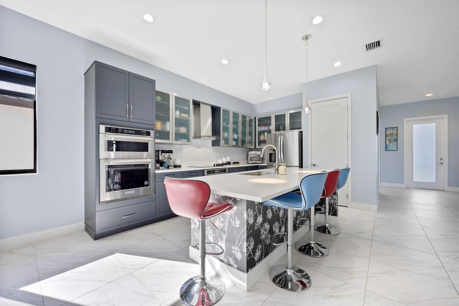 Kitchen featuring glass insert cabinets, decorative light fixtures, a kitchen breakfast bar, a center island with sink, and appliances with stainless steel finishes