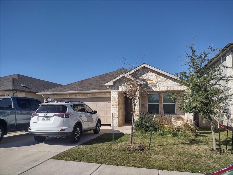 Ranch-style house featuring stone siding, a garage, concrete driveway, a front lawn, and a shingled roof