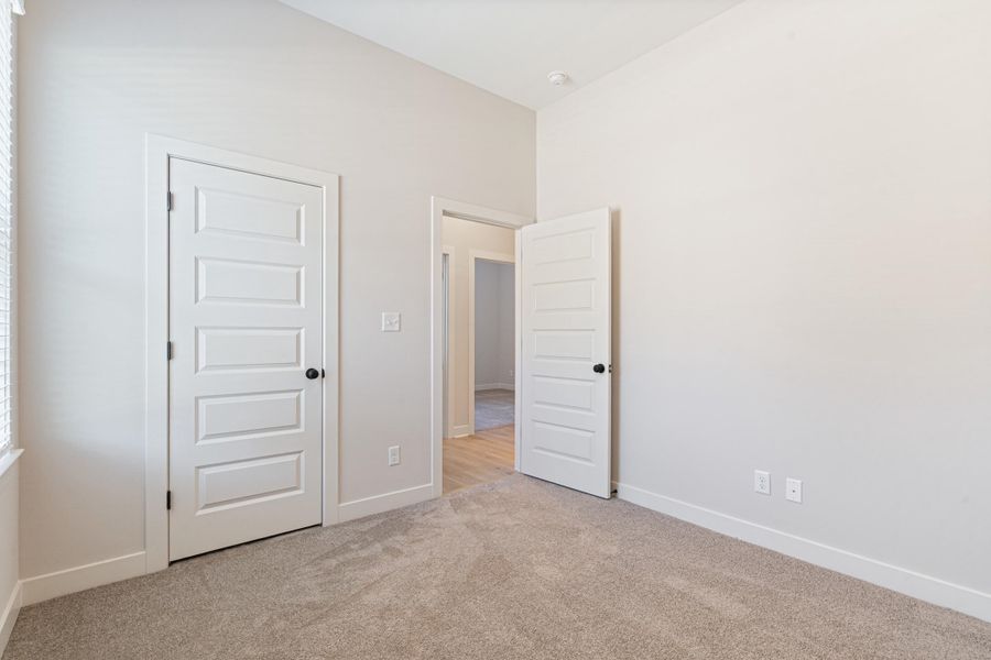 Neutral tone wall color, panel doors with matte black hardware, light-colored carpeting, and window with blinds Neutral tone wall color, panel doors with matte black hardware, light-colored carpeting, and window with blinds