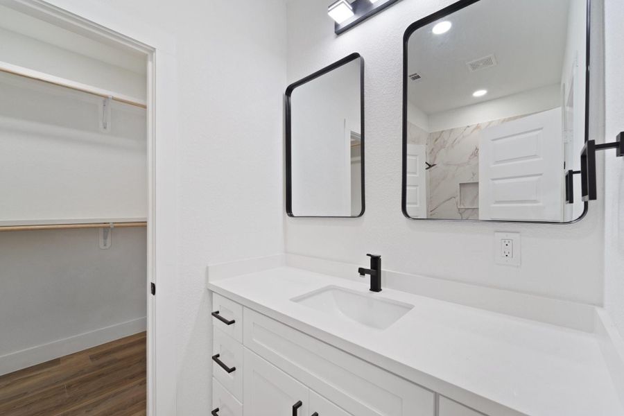 It is complete with framed mirrors, granite countertops and backsplash, and white cabinetry.