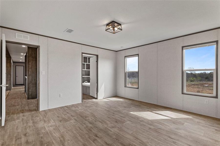 Unfurnished bedroom with light wood-type flooring, crown molding, and ensuite bathroom