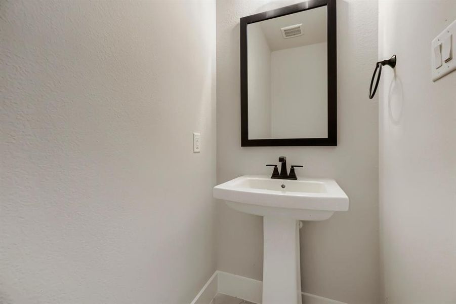 Pedestal sink with a matte black faucet, framed mirror, and a coordinating towel ring