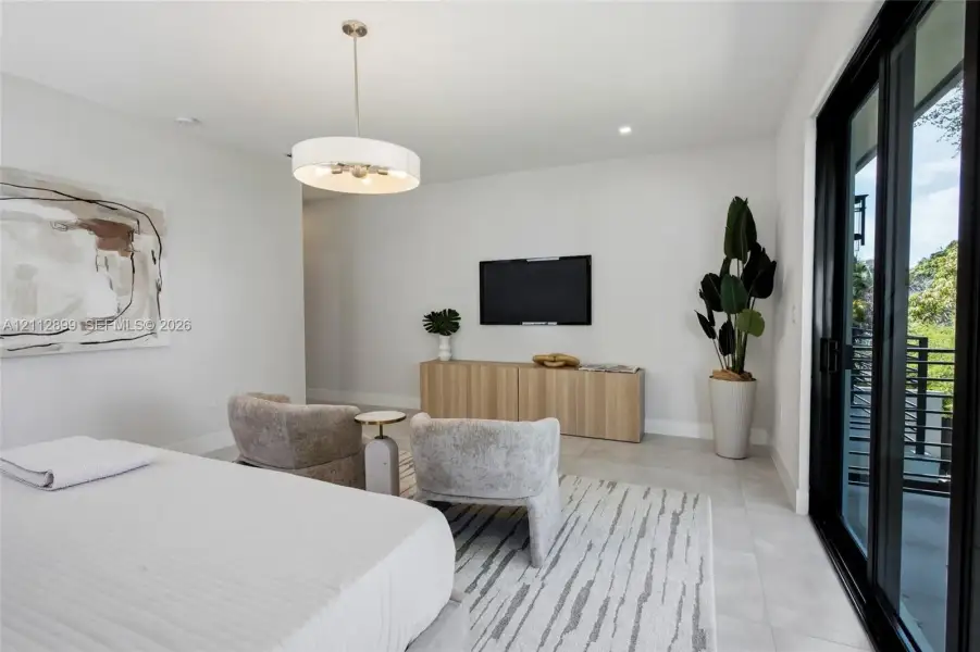 Neutral-toned interior featuring large-format tile flooring, a contemporary drum pendant light fixture, and black-framed sliding glass doors opening to an exterior balcony