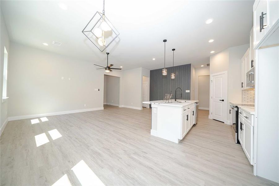 Kitchen featuring white cabinets, a kitchen island with sink, pendant lighting, a ceiling fan, and open floor plan Kitchen featuring white cabinets, a kitchen island with sink, pendant lighting, a ceiling fan, and open floor plan