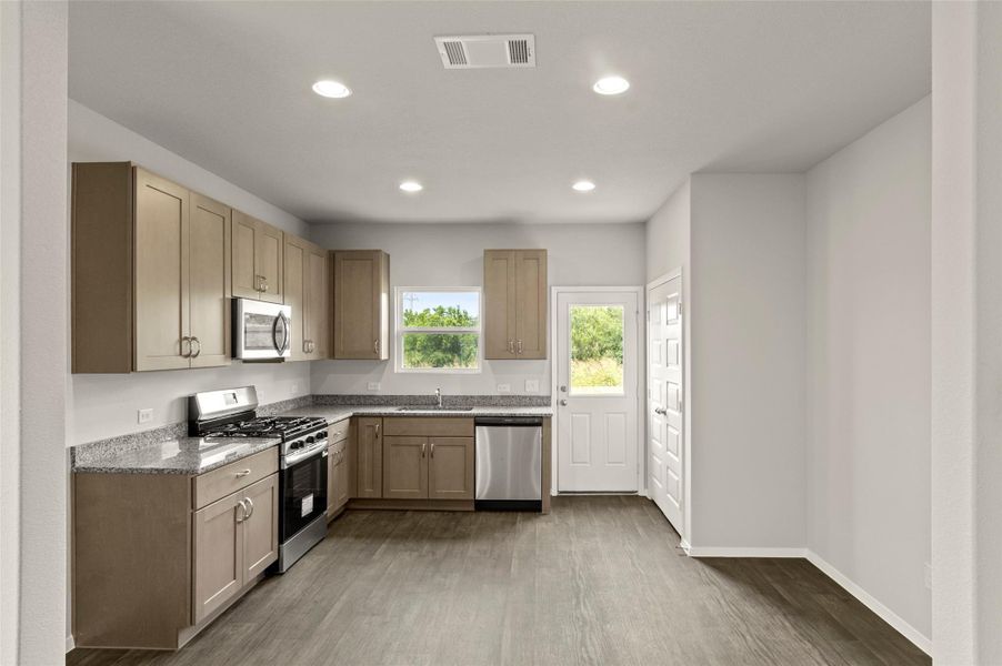 Kitchen with appliances with stainless steel finishes, wood finished floors, recessed lighting, and light stone counters