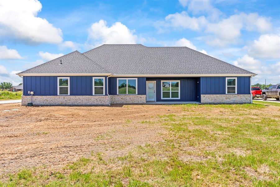 Back of house featuring a shingled roof, board and batten siding, and stone siding