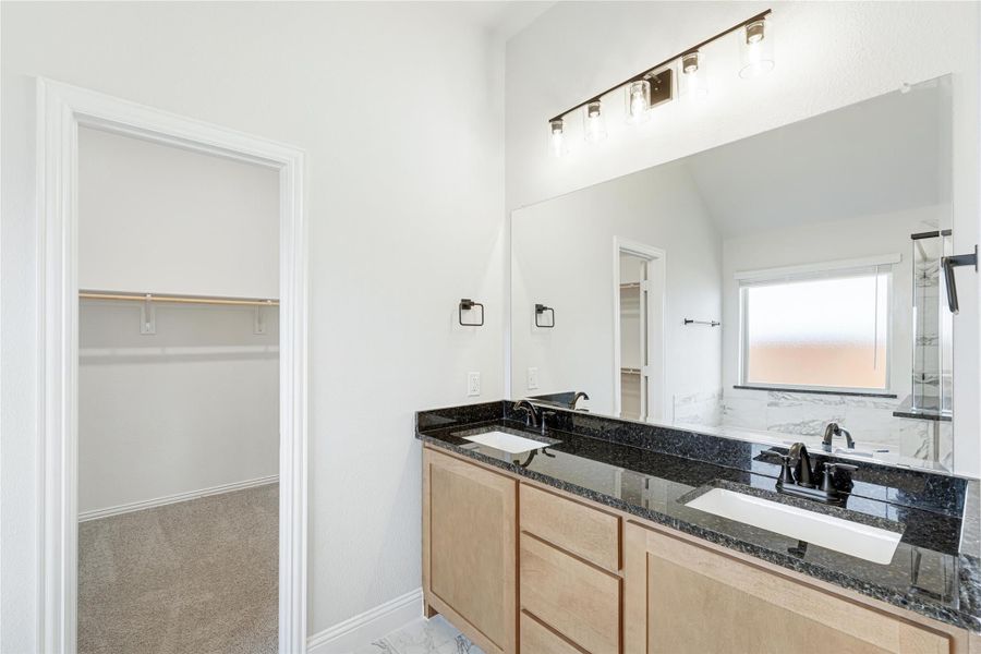 Bathroom with double sink vanity, dark granite countertop, large mirror, and walk-in closet entrance nearby.