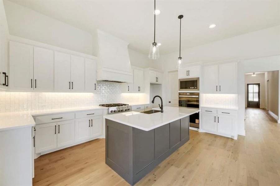 Gourmet kitchen with a large center island, white cabinetry, integrated stainless-steel appliances, and light wood-finish flooring Gourmet kitchen with a large center island, white cabinetry, integrated stainless-steel appliances, and light wood-finish flooring