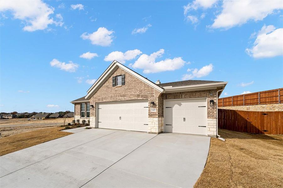 View of front of property with concrete driveway, brick siding, stone siding, and an attached garage