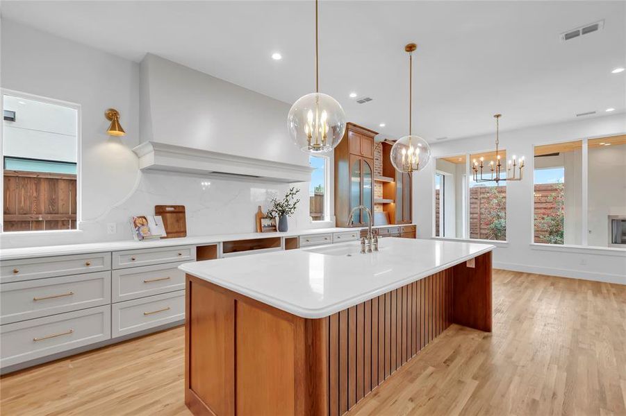 Two tone kitchen featuring two tone cabinets, an island with sink, light wood-type flooring, open shelves, and backsplash