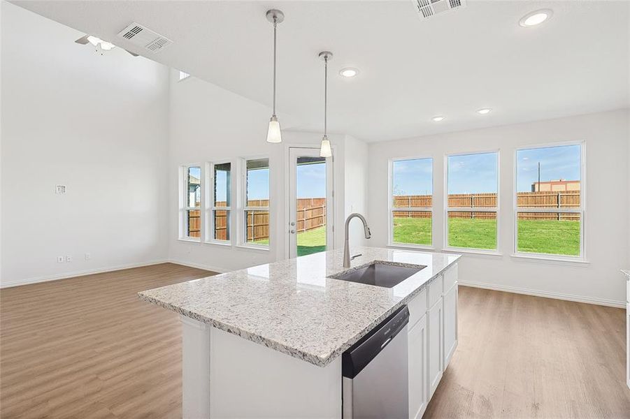 Kitchen featuring sink, light wood-type flooring, dishwasher, decorative light fixtures, and white cabinets