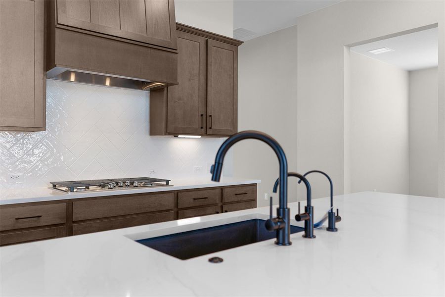 Kitchen with light stone countertops, premium range hood, stainless steel gas cooktop, and tasteful backsplash
