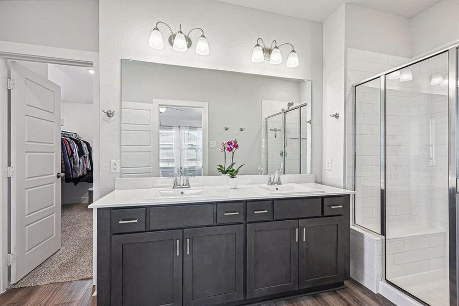 Bathroom with vanity, dual sinks, and a walk in shower with door