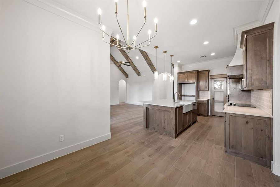 Open-concept living space featuring wood-finish tile flooring, vaulted ceilings with exposed beams, and a modern chandelier