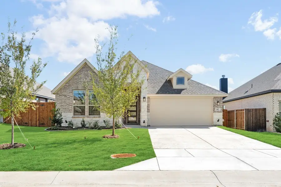 Single-story brick home with two-car garage, concrete driveway, and green front lawn with young trees.
