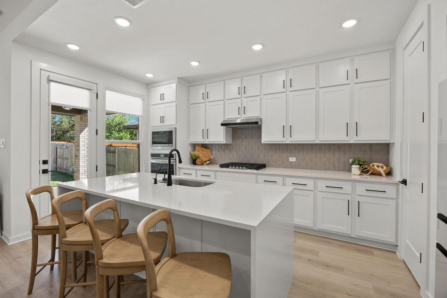 Kitchen with white cabinets, light wood finished floors, a breakfast bar, light stone counters, and recessed lighting