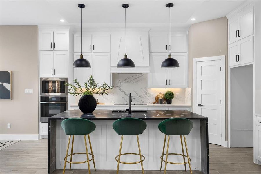 Kitchen featuring pendant lighting, stainless steel oven, a kitchen island with sink, white cabinets, and decorative backsplash