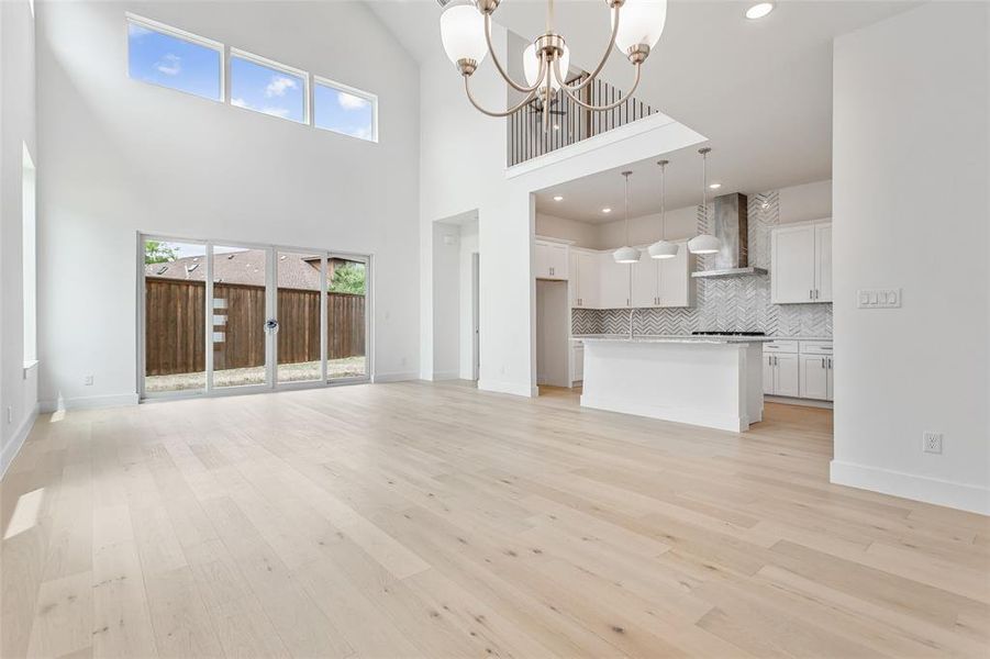 Unfurnished living room featuring light wood-type flooring, an inviting chandelier, and a towering ceiling