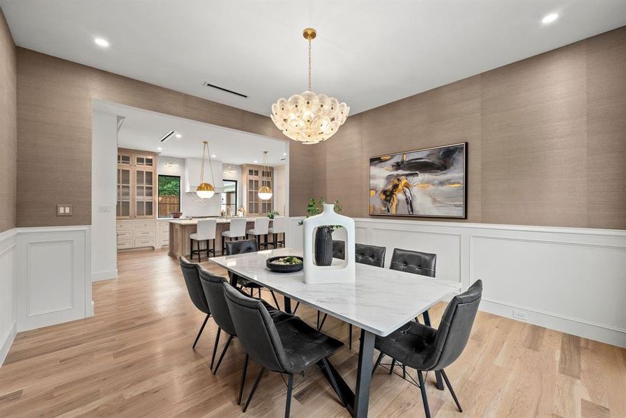 Dining area featuring light hardwood flooring, wainscoting, and a decorative chandelier