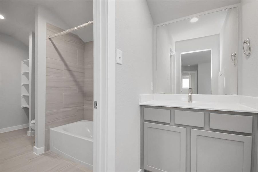 Secondary bathroom, designed for Jack and Jill arrangements, now with a separate vanity area. This well-appointed space showcases stylish tile flooring, a bath/shower combo with an elegant tile surround, and slate colored wood cabinets. Sample photo of completed home with similar floor plan. Actual colors and selections may vary.