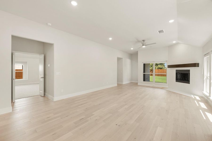 Open living room with light hardwood floors, fireplace, ceiling fan, and vaulted ceiling