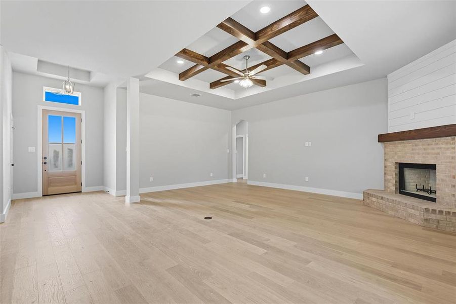 Unfurnished living room with coffered ceiling, light wood-style flooring, beamed ceiling, a fireplace, and ceiling fan Unfurnished living room with coffered ceiling, light wood-style flooring, beamed ceiling, a fireplace, and ceiling fan
