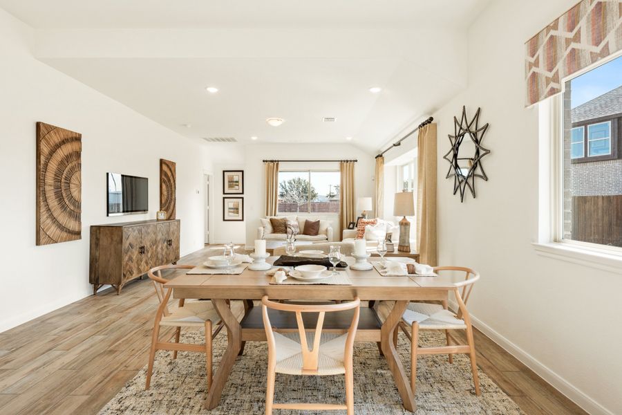 Open-concept dining area with wood table and chairs flowing into a living room with hardwood floors and natural light