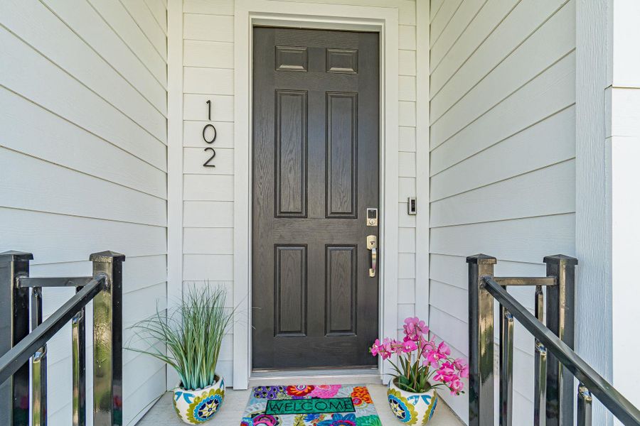 A dark paneled door welcomes guests, flanked by vibrant planters and a clean exterior. A dark paneled door welcomes guests, flanked by vibrant planters and a clean exterior.