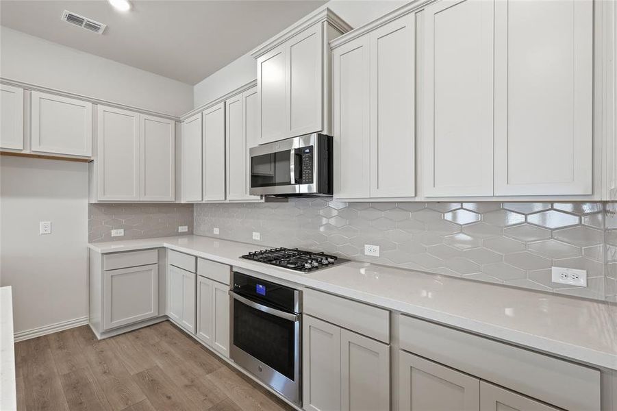Kitchen featuring stainless steel appliances, backsplash, light wood-type flooring, and white cabinetry