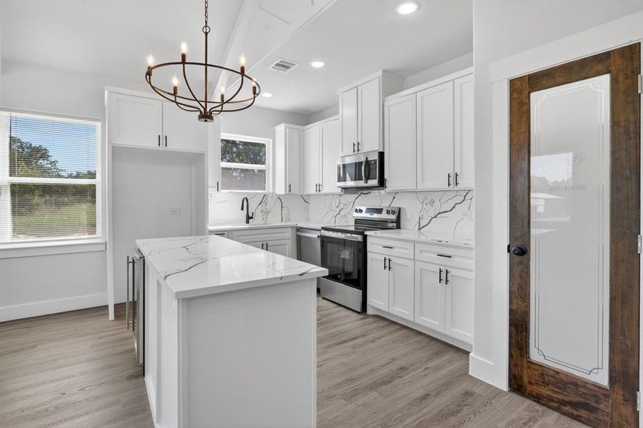 Contemporary kitchen featuring white cabinetry, stainless steel appliances, a central island with a waterfall countertop, and wood-finish flooring