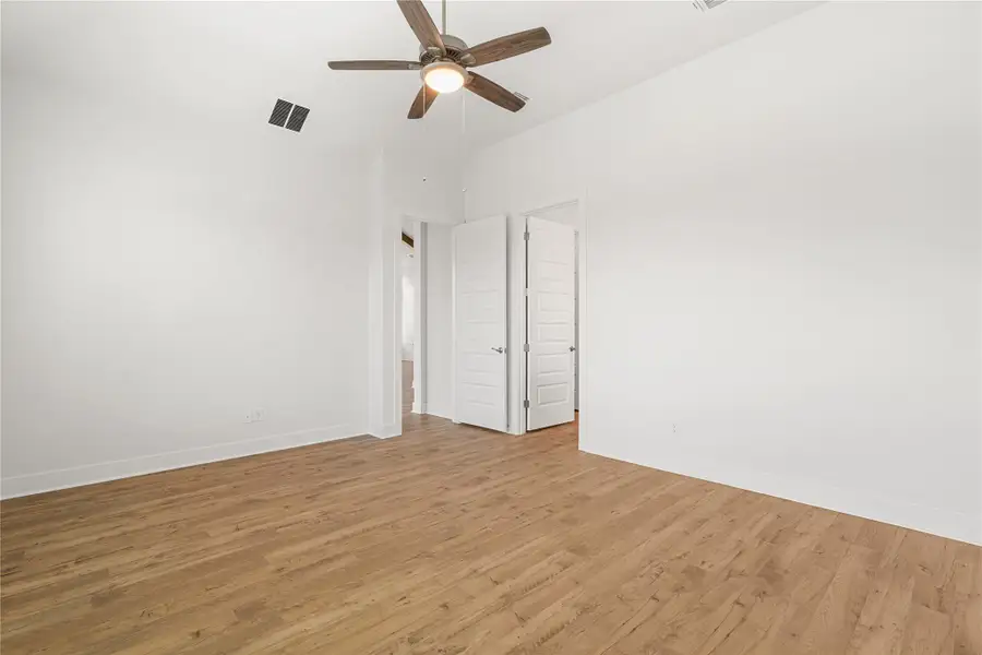 A well-lit bedroom features wood flooring, a ceiling fan, and access to a walk-in closet. A well-lit bedroom features wood flooring, a ceiling fan, and access to a walk-in closet.