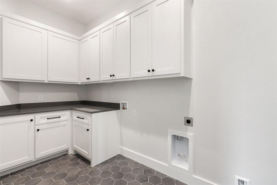 Modern laundry room featuring abundant white cabinetry, sleek countertops, and practical hexagonal tile flooring.