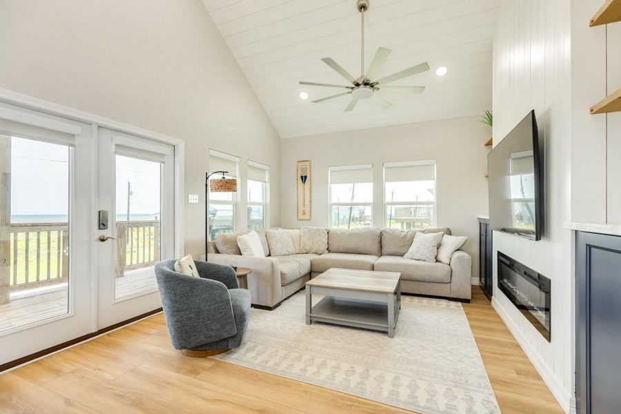 Bright, open-concept living room features soaring vaulted ceilings, expansive windows, and direct access to the covered balcony, creating a welcoming space for relaxing or entertaining.