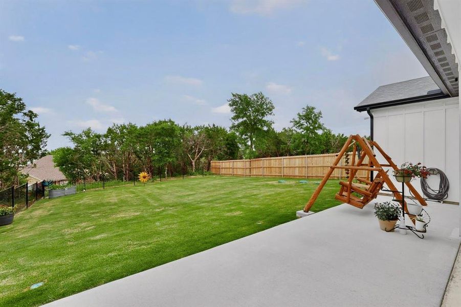 Expansive backyard featuring a concrete patio, a wooden privacy fence, and a black wrought iron fence
