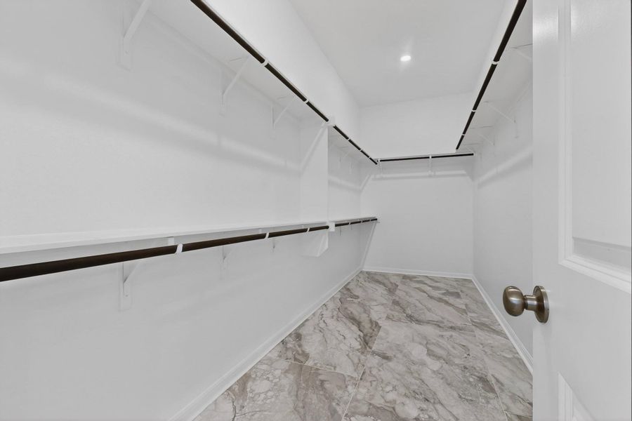 Walk-in closet featuring white wire shelving, dark hanging rods, recessed ceiling lighting, and grey patterned tile flooring