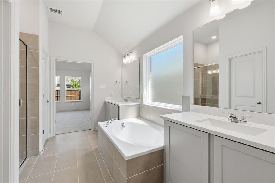 Full bathroom featuring vaulted ceiling, two vanities, a shower stall, a bath, and light tile patterned floors